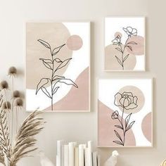 three framed art prints on the wall above a table with books and flowers in vases