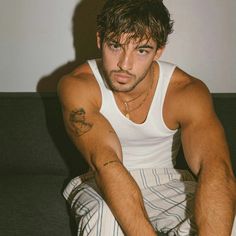 a man sitting on top of a couch with his hands in his pockets and tattoos on his arm