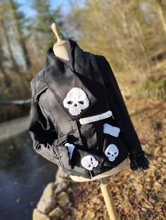 a black jacket with skulls and bones on it is hanging from a wooden stand in front of a body of water