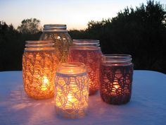 four mason jars sitting on top of a snow covered table with lit candles in them