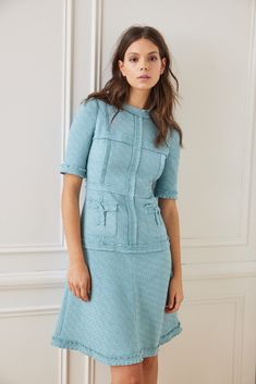 a woman standing in front of a white wall wearing a blue dress with pockets on the side