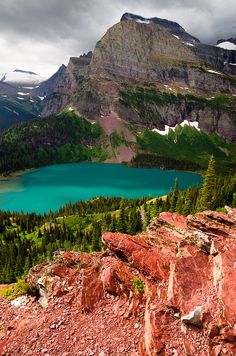 a lake surrounded by mountains and trees on a cloudy day