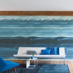 a living room with blue chairs and a white couch in front of a large painting on the wall