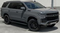 a silver truck parked in front of a white building with black rims on it's tires