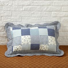 a blue and white checkered pillow sitting on top of a wooden table next to a brick wall