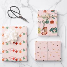 wrapping paper and scissors on a marble countertop with pink wrapping paper, white ribbon, and orange polka dots