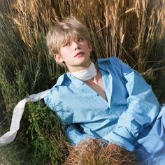 a young man sitting in the grass wearing a blue shirt and tie