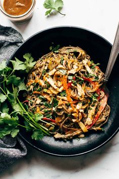 a black plate topped with noodles and veggies next to a bowl of sauce