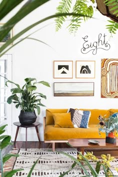 a living room filled with lots of plants and pictures on the wall above it's couch