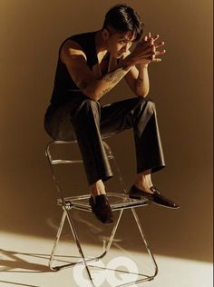 a man sitting on top of a chair with his hands clasped to his chest and legs crossed