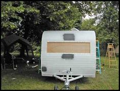 an old camper trailer is parked in the grass near some trees and ladders