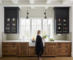 a woman standing in front of a kitchen sink with black cabinets and white counter tops