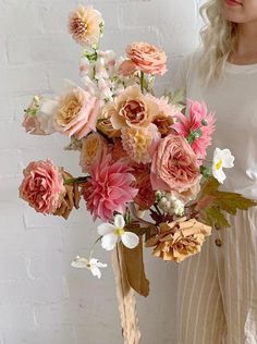 a woman standing next to a white brick wall holding a bouquet of pink and yellow flowers