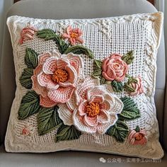 a white pillow with pink flowers on it sitting on a gray chair in front of a window