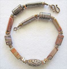 The romance of the beautiful Sonora Desert of the Southwest is how Miriam describes the softly flowing shades of the Jasper beads she used to create a necklace that is sure to bring compliments. Each bead shows a unique pattern of swirling soft and romantic waves grays, taupes, deep terra cotta reds, and the soft mauves that are typical of natural Imperial and Brown Jaspers. Accent beads are jasper and handwrought bronze beads add to the distinctive beauty of the necklace. The pendant bronze, al Flower Jade, Jewelry Knowledge, Beaded Things, Jewelry Stones, Beaded Necklace Designs, Necklace Ideas, Bronze Necklace, Romantic Colors, Trendy Nail