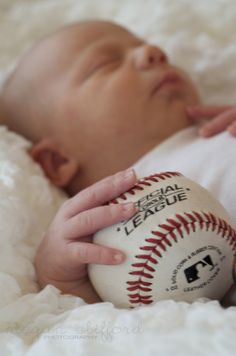 a close up of a baby holding a baseball in it's hand while laying on a bed