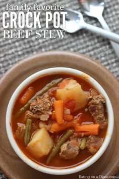 a bowl of stew with meat, potatoes and green beans on a plate next to a fork