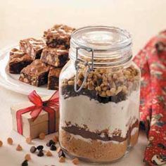 a glass jar filled with desserts next to a plate of cookies and chocolate bars