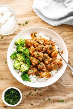 a white bowl filled with chicken and broccoli on top of rice next to sauce