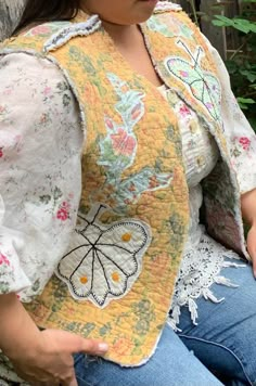 a woman sitting on a bench wearing a yellow jacket with butterfly appliqued on it