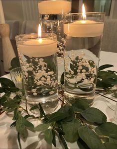 two candles sitting on top of a table with greenery and flowers in the middle