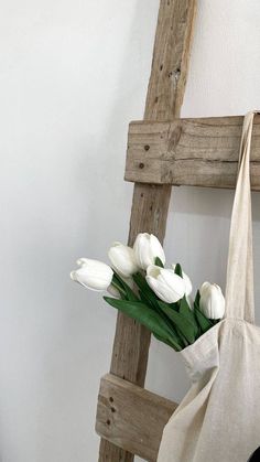 white tulips in a bag sitting on a chair next to a wooden ladder