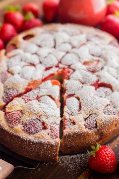 a strawberry cake with powdered sugar on top and strawberries around the edges, ready to be eaten