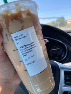 a person holding up a plastic cup filled with liquid in the passenger seat of a car