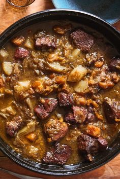 a bowl filled with meat and potatoes on top of a wooden table next to glasses