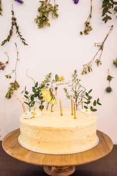 a cake with flowers and plants on top is sitting on a wooden stand in front of a white wall