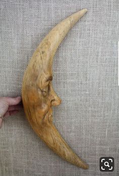 a wooden crescent moon with a human face carved into it's side, being held by a hand