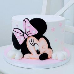 a minnie mouse cake with pink and white icing on a chair in the background