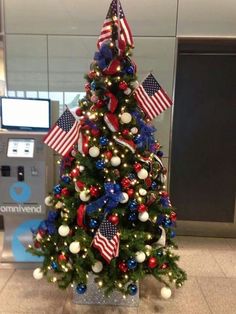 a decorated christmas tree with red, white and blue decorations in an airport terminal lobby