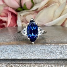 a blue and white diamond ring sitting on top of a wooden table next to flowers