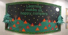 a bulletin board that says learning makes us happy campers with trees and stars on it