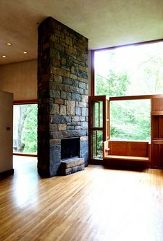 an empty living room with wood floors and a stone fireplace in the center, surrounded by large windows