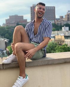 a man sitting on top of a cement wall next to a tall building with buildings in the background