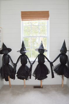 four plastic witches sitting on top of wooden sticks in front of a window with a white wall