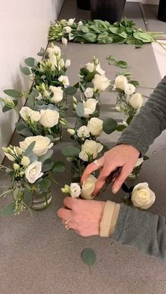 a person cutting flowers with scissors on a table next to other flowers and greenery