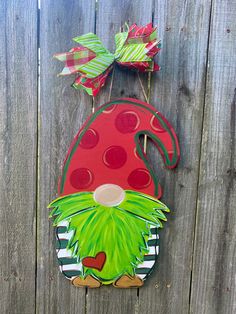 a red and green gnome door hanger on a wooden fence with two bows attached to it