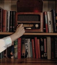 a person reaching for an old radio on a book shelf