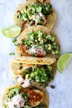 four tacos with different toppings on them and lime wedges next to each other