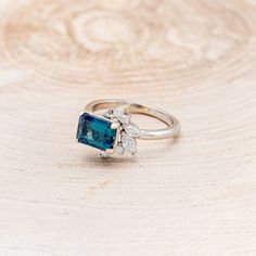 an engagement ring with a blue stone surrounded by white diamonds on a wooden background,