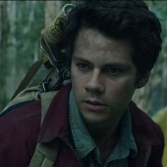 a young man with a backpack on his back in the woods, staring at the camera