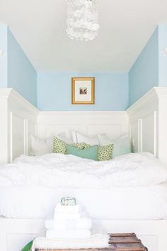 a white bed sitting under a chandelier next to a wooden table and chair