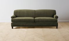 a green couch sitting on top of a hard wood floor next to a white wall