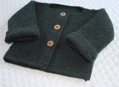 a green knitted sweater laying on top of a bed