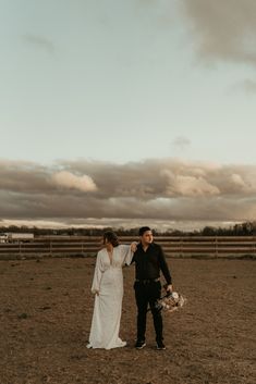 a man and woman standing in an open field next to each other with clouds in the background