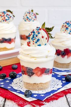 three dessert cups with strawberries, blueberries and whipped cream in them on a patriotic table cloth