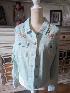 a light blue jean jacket with floral appliques on the front and back, sitting on a mannequin